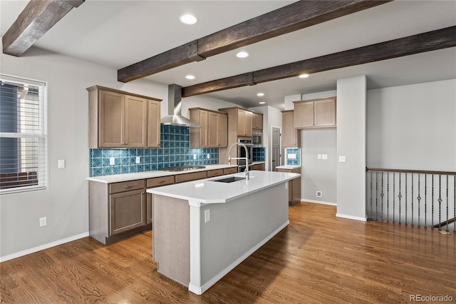 kitchen with wall chimney exhaust hood, sink, dark hardwood / wood-style flooring, stainless steel gas stovetop, and a kitchen island with sink