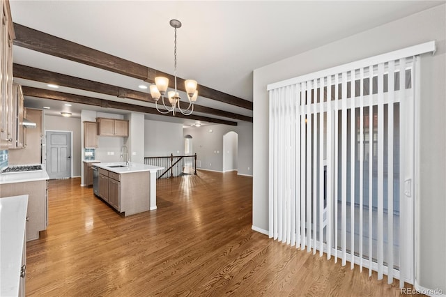 kitchen featuring an inviting chandelier, hardwood / wood-style floors, an island with sink, decorative light fixtures, and beamed ceiling