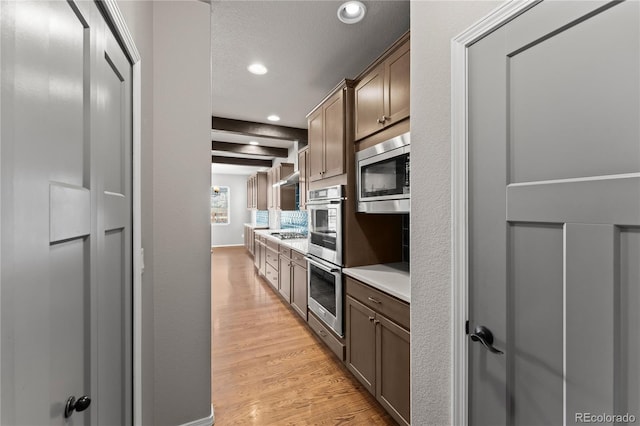 kitchen featuring a textured ceiling, light hardwood / wood-style flooring, stainless steel appliances, and beamed ceiling