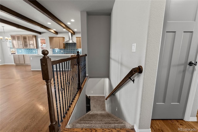 stairway with hardwood / wood-style floors, a notable chandelier, and beam ceiling