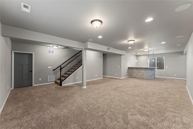 basement featuring carpet floors, a textured ceiling, and indoor bar