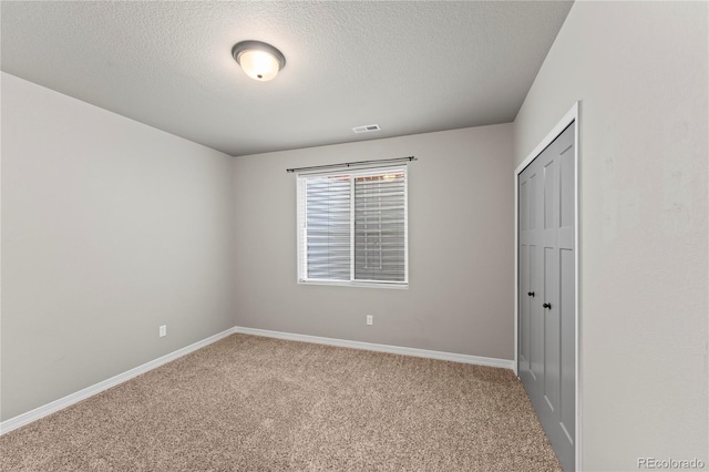 unfurnished bedroom featuring light colored carpet, a textured ceiling, and a closet