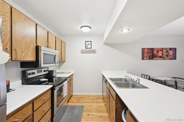 kitchen with a sink, stainless steel appliances, light wood-style floors, a peninsula, and light countertops