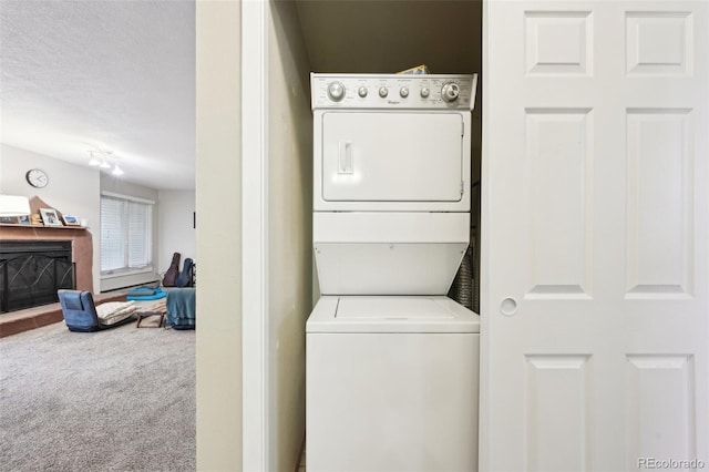 laundry room featuring carpet floors, stacked washing maching and dryer, laundry area, a fireplace, and a textured ceiling