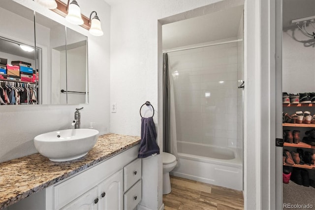 bathroom featuring toilet, vanity, wood finished floors, a spacious closet, and shower / bathing tub combination