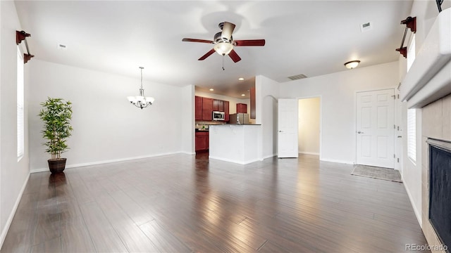 unfurnished living room featuring ceiling fan with notable chandelier, a fireplace, baseboards, and dark wood-style flooring