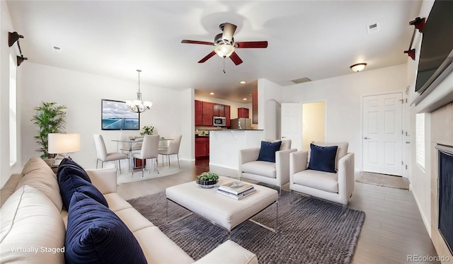 living area featuring ceiling fan with notable chandelier, recessed lighting, light wood-style floors, and visible vents