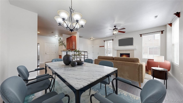 dining room featuring a tiled fireplace, plenty of natural light, ceiling fan with notable chandelier, and visible vents