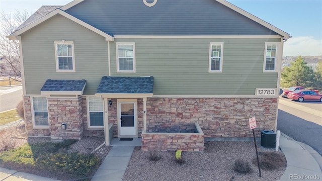 view of front of house with central AC, stone siding, and roof with shingles