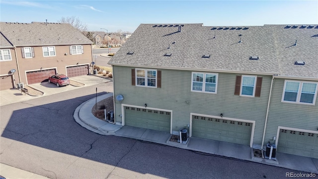 back of property featuring cooling unit, an attached garage, and roof with shingles