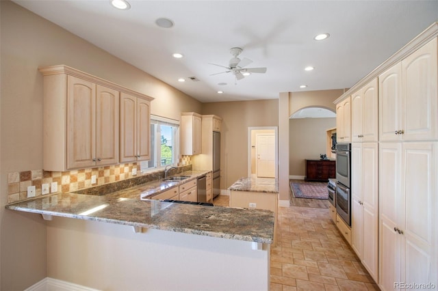 kitchen with kitchen peninsula, ceiling fan, appliances with stainless steel finishes, light stone countertops, and sink