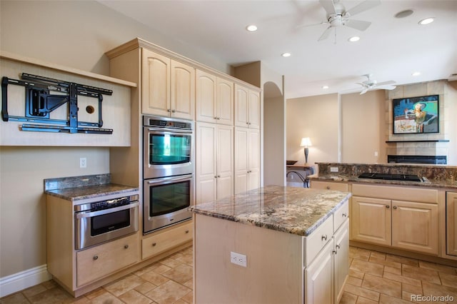 kitchen with ceiling fan, a kitchen island, double oven, and stone countertops