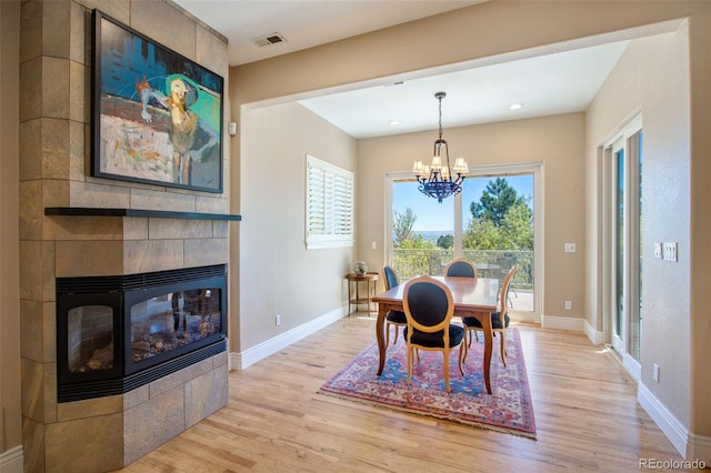 dining area with an inviting chandelier, light wood-type flooring, a healthy amount of sunlight, and a fireplace