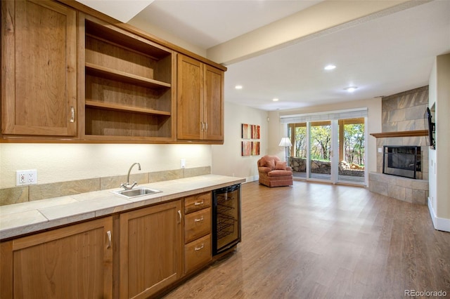 kitchen featuring tile counters, a tiled fireplace, beverage cooler, light hardwood / wood-style flooring, and sink