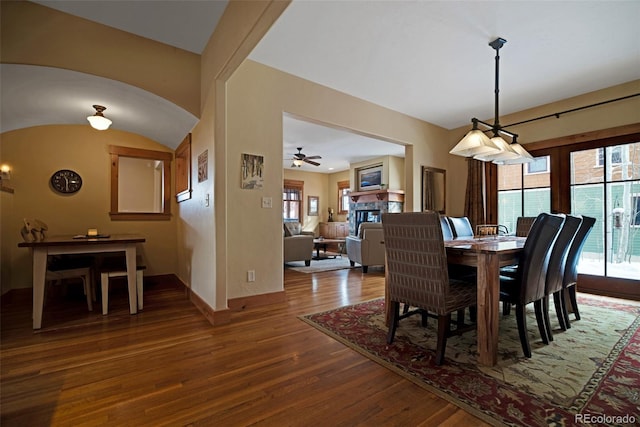 dining area featuring arched walkways, a fireplace, a ceiling fan, wood finished floors, and baseboards