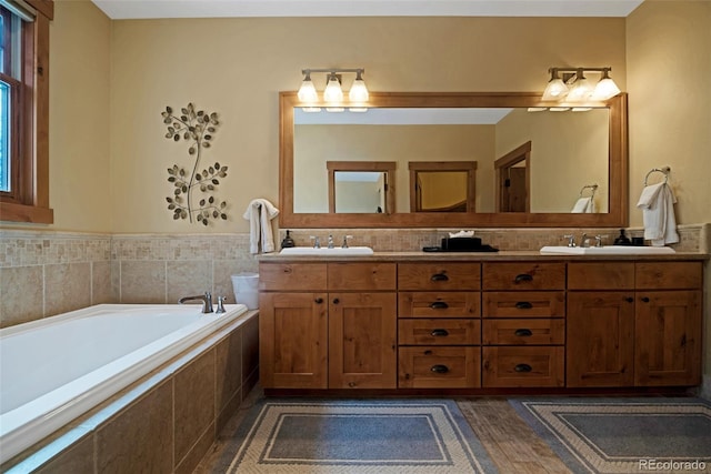 full bathroom featuring a bath, double vanity, a sink, and wood finished floors