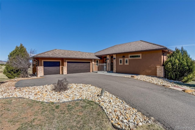 view of front facade featuring stucco siding, a garage, stone siding, aphalt driveway, and a tiled roof