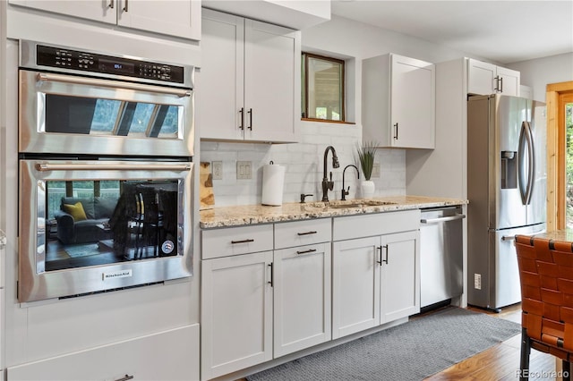 kitchen with decorative backsplash, a sink, light stone counters, light wood finished floors, and stainless steel appliances