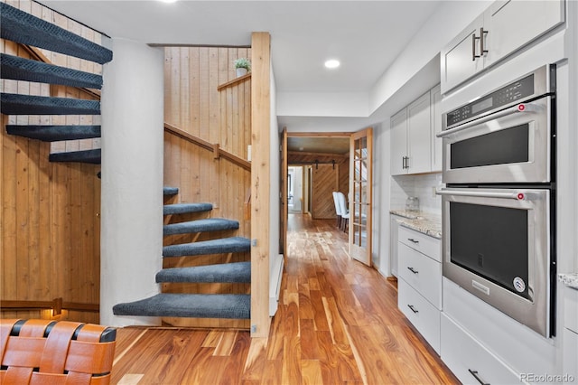 kitchen with double oven, white cabinets, light stone countertops, and light wood-type flooring