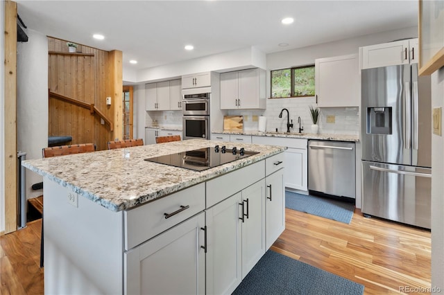 kitchen with a kitchen island, tasteful backsplash, a sink, light wood-style floors, and stainless steel appliances