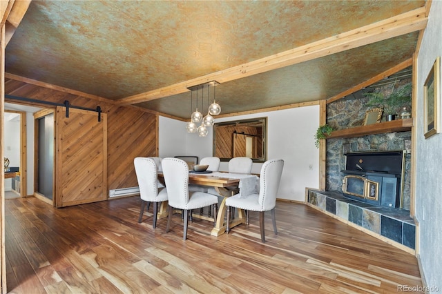 dining space with hardwood / wood-style floors, baseboards, wooden walls, baseboard heating, and a barn door