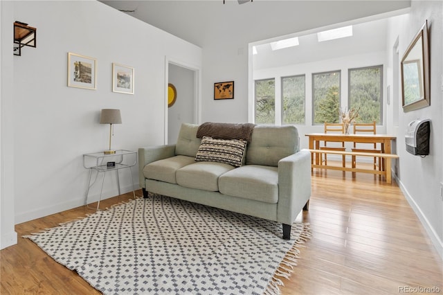 living room with a skylight, baseboards, and light wood-style flooring