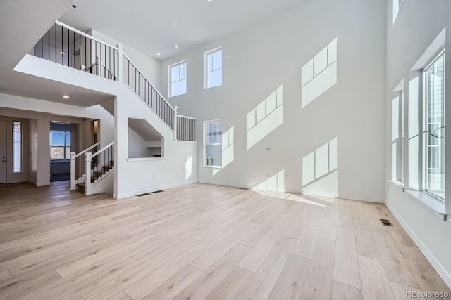 unfurnished living room featuring light wood-type flooring and a towering ceiling