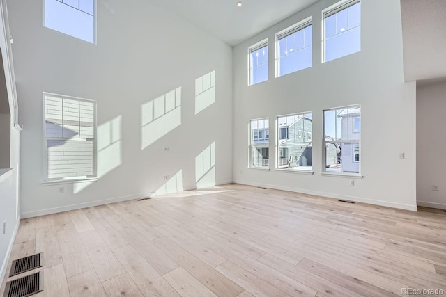 unfurnished living room with a towering ceiling and light wood-type flooring