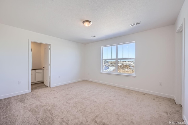 unfurnished bedroom with connected bathroom, light colored carpet, and a textured ceiling