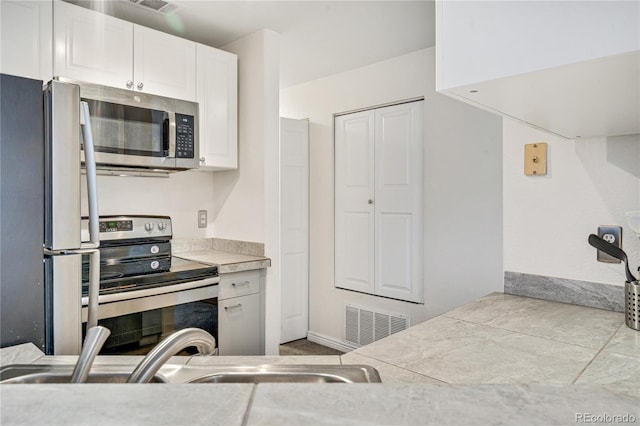 kitchen featuring stainless steel appliances, white cabinetry, light countertops, and a sink