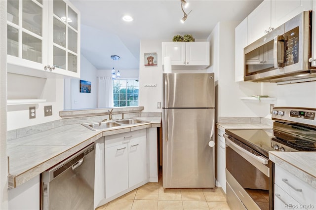 kitchen with appliances with stainless steel finishes, a sink, light countertops, white cabinets, and glass insert cabinets