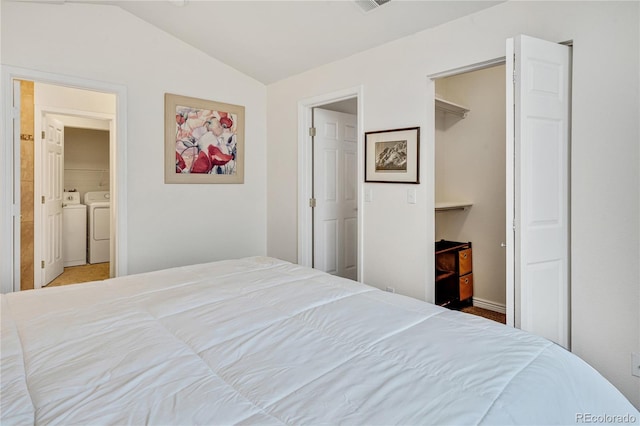 bedroom featuring washing machine and clothes dryer, lofted ceiling, a walk in closet, connected bathroom, and baseboards