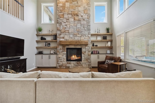 living room featuring a towering ceiling, plenty of natural light, wood finished floors, and a fireplace