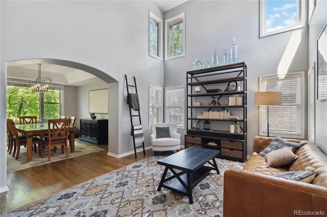 living room with arched walkways, wood finished floors, a high ceiling, baseboards, and a chandelier
