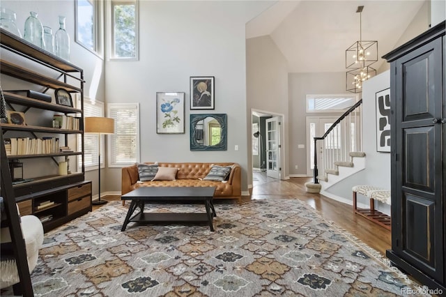 sitting room with high vaulted ceiling, plenty of natural light, a chandelier, stairway, and baseboards