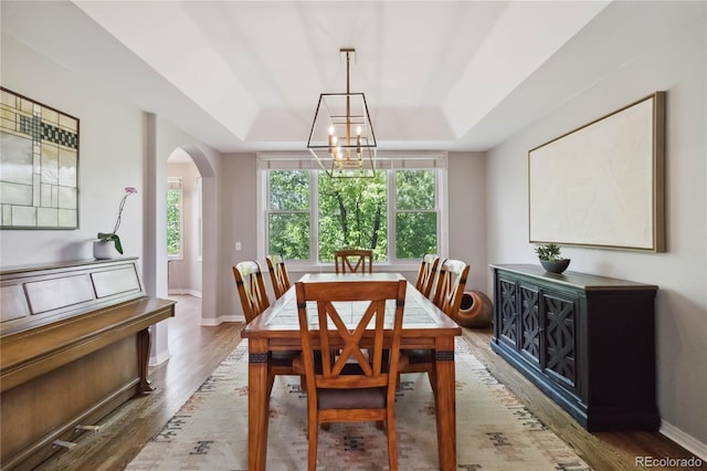 dining area with a tray ceiling, arched walkways, wood finished floors, a chandelier, and baseboards