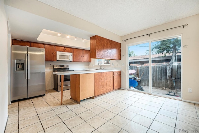 12662 W Virginia Ave, Lakewood, CO 80228 - kitchen with a peninsula, stainless steel appliances, brown cabinetry, light countertops, and light tile patterned flooring