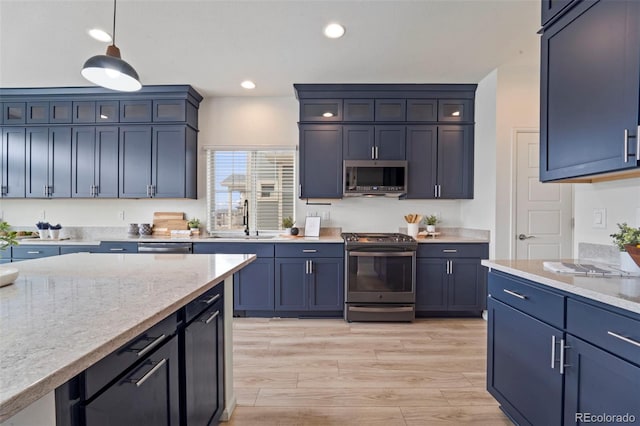 kitchen with a sink, appliances with stainless steel finishes, light wood-type flooring, light stone countertops, and decorative light fixtures