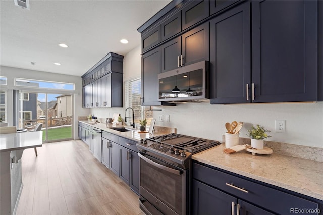 kitchen featuring appliances with stainless steel finishes, light wood-style floors, a sink, and light stone counters