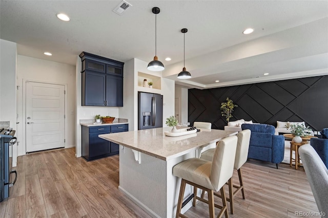 kitchen featuring visible vents, light wood-style floors, a kitchen breakfast bar, open floor plan, and black appliances