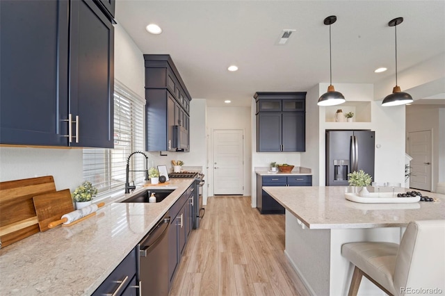 kitchen with stainless steel appliances, visible vents, light wood-style floors, a sink, and light stone countertops