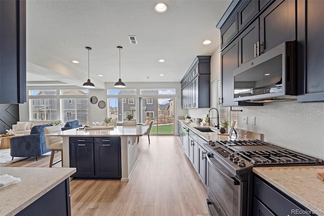 kitchen featuring light wood-style flooring, a kitchen island, open floor plan, stainless steel appliances, and a sink