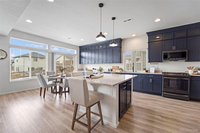 kitchen featuring stainless steel appliances, a breakfast bar, visible vents, light wood-style floors, and a center island