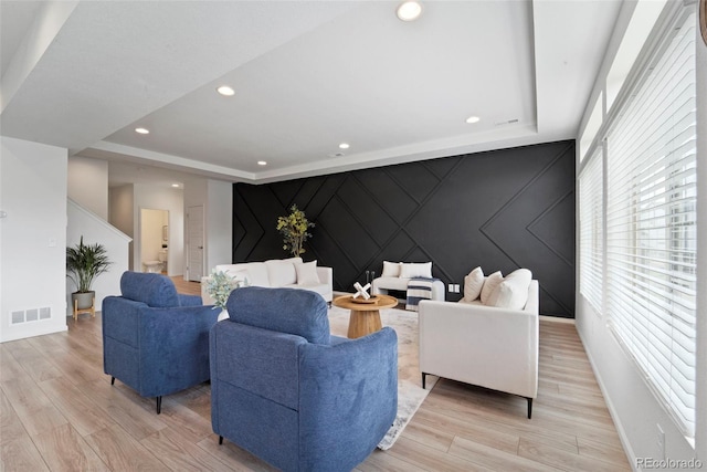 living area featuring an accent wall, a tray ceiling, light wood-type flooring, and visible vents