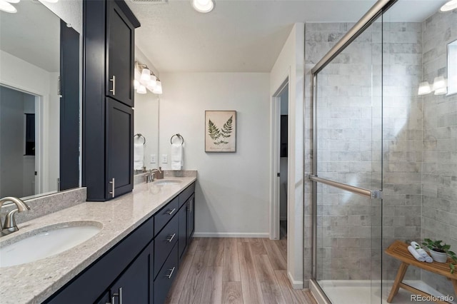 full bath featuring a stall shower, double vanity, a sink, and wood finished floors