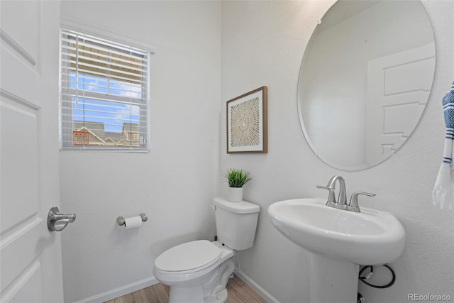 half bath featuring baseboards, a sink, toilet, and wood finished floors