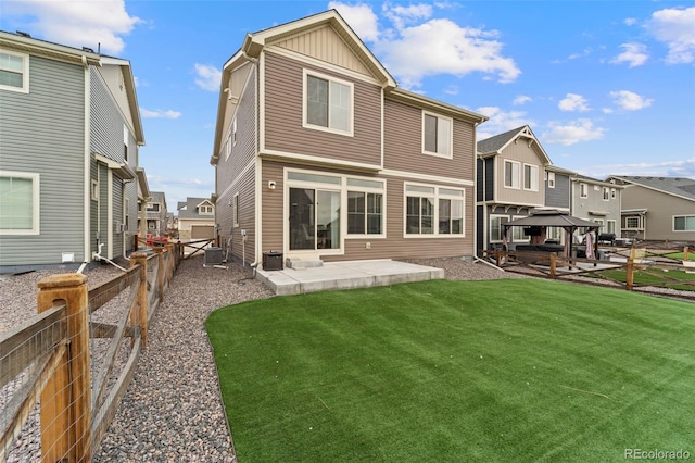 rear view of house with a lawn, a gazebo, board and batten siding, a patio area, and a fenced backyard