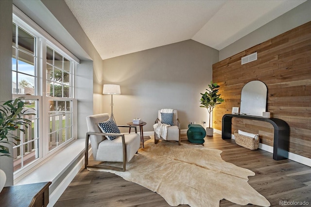 sitting room featuring vaulted ceiling, wood walls, baseboards, and visible vents