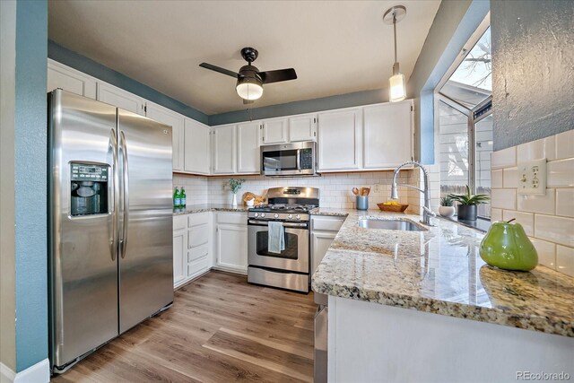 kitchen with tasteful backsplash, a sink, light stone counters, white cabinets, and stainless steel appliances