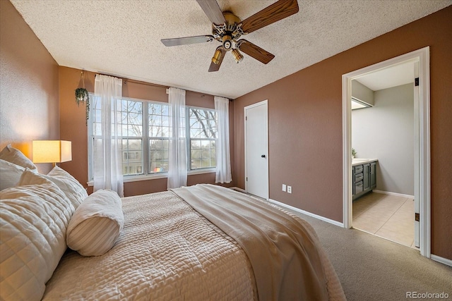 bedroom featuring baseboards, ensuite bathroom, ceiling fan, light colored carpet, and a textured ceiling